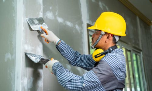 Worker repairs wall,Construction industry worker using a putty knife and leveling in house under reconstruction.